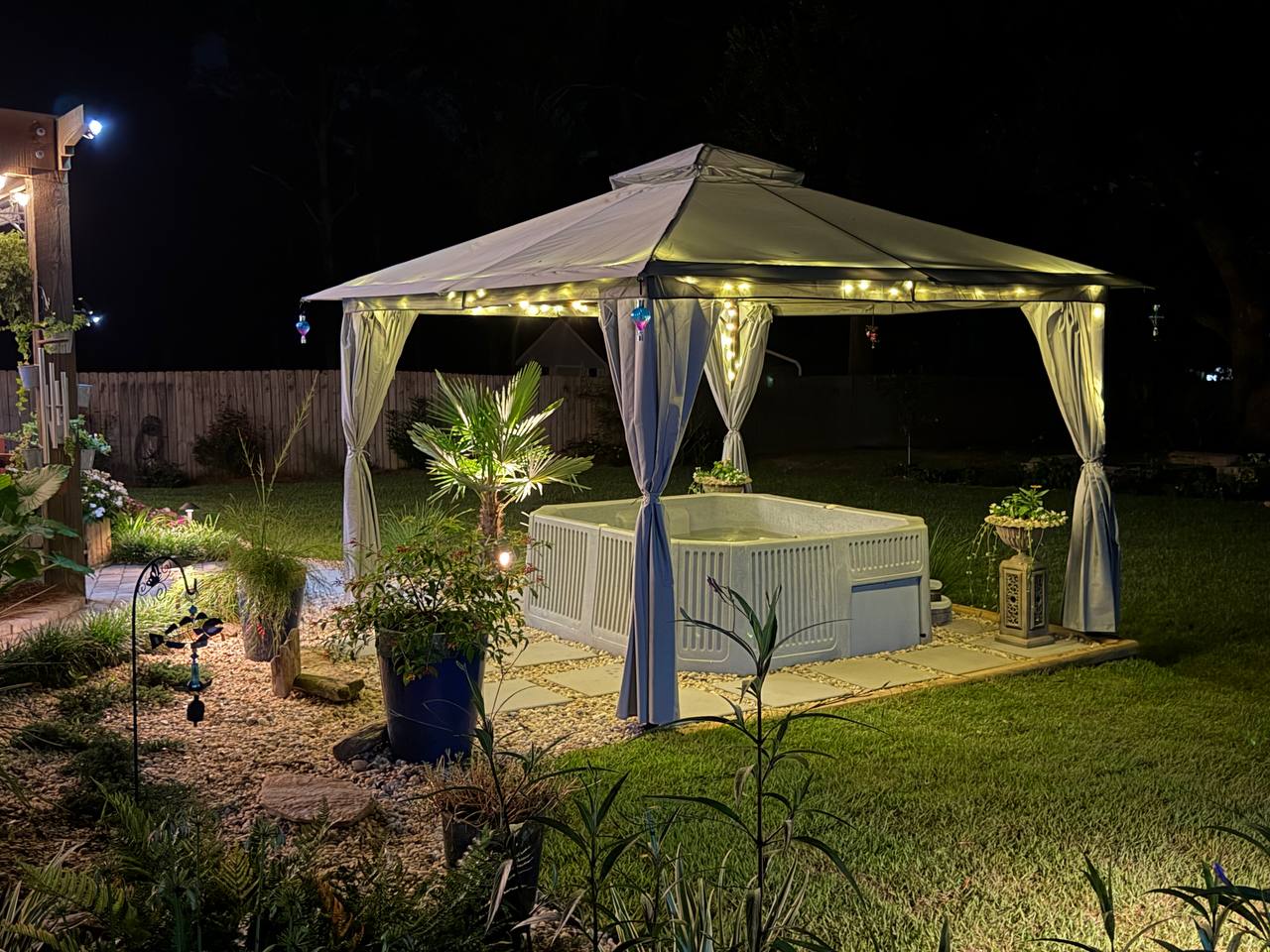 Backyard spa garden glowing beneath a lit canopy beside a winding path and planted beds